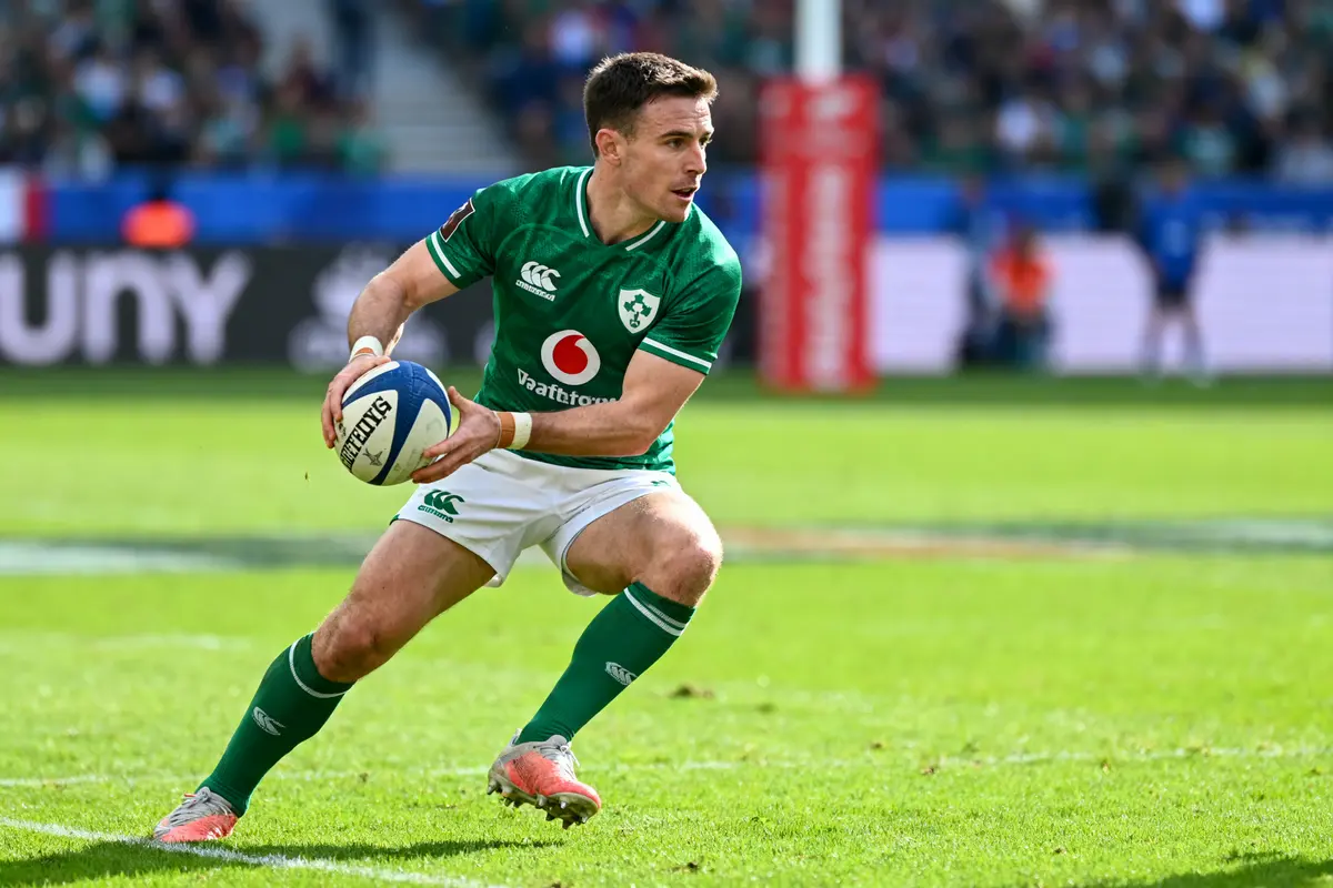 Joueur de rugby en action, portant un maillot vert, tenant un ballon sur un terrain de jeu en extérieur.